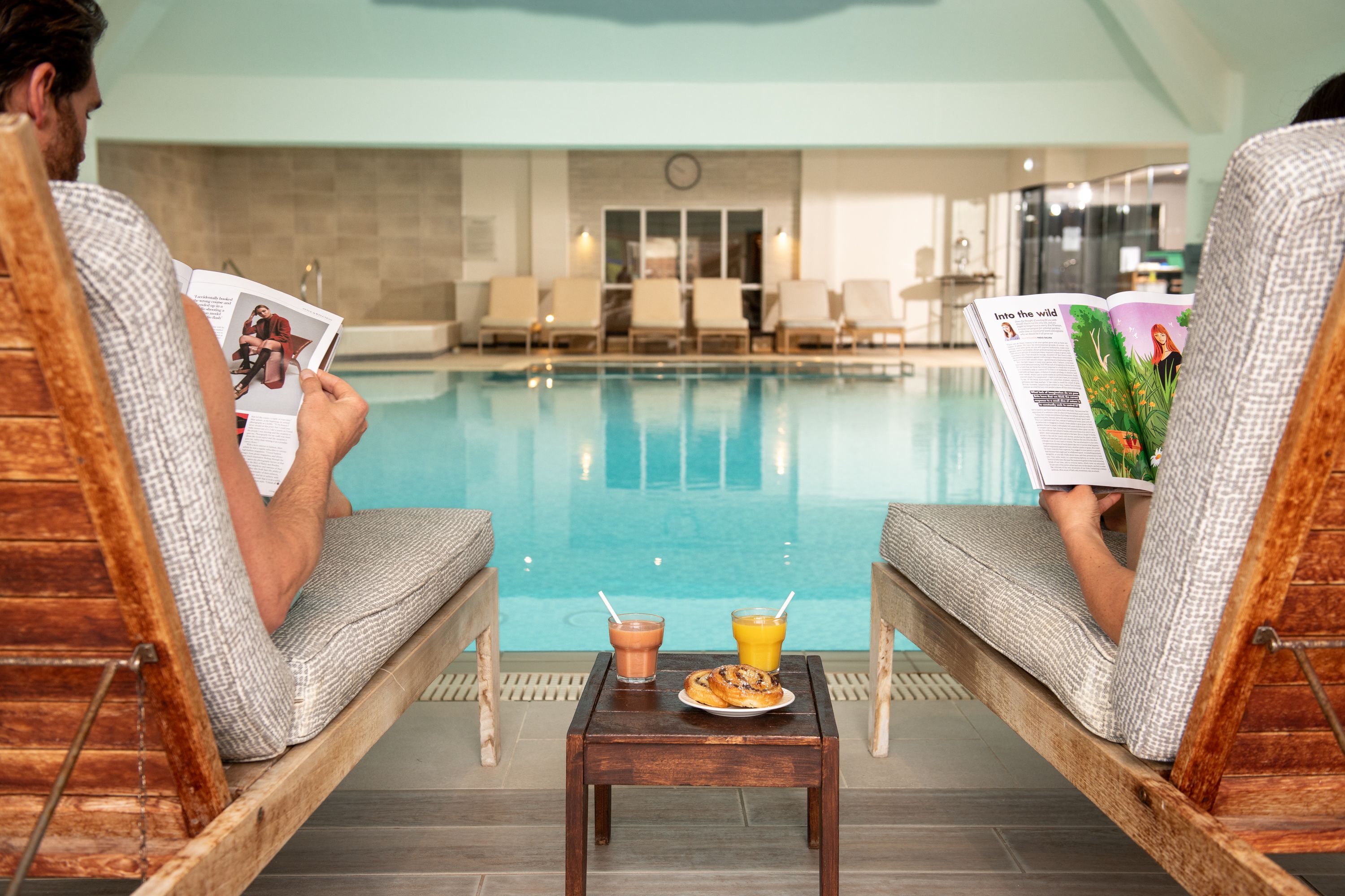 A man and woman reading a magazine in front of the pool
